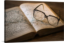  This print is a captivating photograph of an open book with a pair of modern, black glasses resting on it. The book is open to a map of Europe, making this print a perfect piece for those who harbor a love for travel or geography.