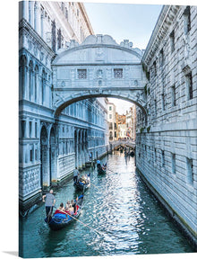  Immerse yourself in the serene beauty of Venice with this exquisite print. The artwork captures a timeless moment along the iconic canals, where gondolas gracefully navigate the tranquil waters beneath an architecturally stunning bridge. The intricate details of the historic buildings, bathed in soft sunlight, transport you right into the heart of an unforgettable moment.