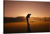 The photograph features the silhouette of a golfer, mid-swing, against the backdrop of an orange sky. The tranquil golf course, with trees and mountains in the distance, adds depth to the scene. The rising sun casts a warm glow, creating a sense of peace and tranquility. 