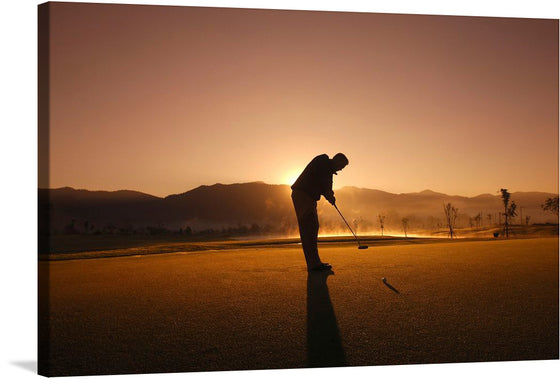 The photograph features the silhouette of a golfer, mid-swing, against the backdrop of an orange sky. The tranquil golf course, with trees and mountains in the distance, adds depth to the scene. The rising sun casts a warm glow, creating a sense of peace and tranquility. 