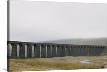  Introducing “Ribblehead Viaduct, UK,” a print that captures the serene beauty of an iconic stone viaduct stretching gracefully across a tranquil landscape. Each meticulously crafted arch stands as a testament to architectural prowess, inviting viewers into a world where human ingenuity meets natural splendor. The misty backdrop and lush grasslands evoke a sense of timeless elegance and peaceful solitude. 