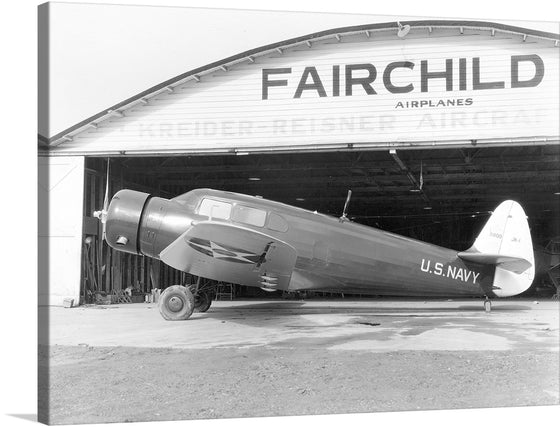 This black and white photograph captures the timeless beauty of the Fairchild JK-1, a small, propeller-driven aircraft that was developed by Fairchild Aviation in the early 1900s. The aircraft is shown parked outside a Fairchild Airplanes hangar, with its sleek lines and elegant design on full display.