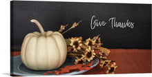  “Give Thanks” is a delightful print that captures the essence of the fall season. The artwork features a white pumpkin resting on a blue plate, surrounded by autumnal flowers in hues of orange and yellow. The dark, chalkboard-like background provides a striking contrast, making the colors pop. The whimsical script of “Give Thanks” written in white adds a touch of charm to the piece. 