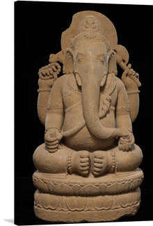  This is a stone sculpture of a potbellied, elephant-headed figure with four arms. The figure is seated in a meditative posture on an ornately carved base. Each hand holds different symbolic objects. The texture of the stone is visible, indicating intricate craftsmanship. 