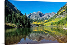  This stunning print of a mountain landscape with a lake in the foreground is sure to take your breath away. The mountains are snow-capped and have a mix of green and yellow trees. The lake is calm and reflects the mountains and trees. 