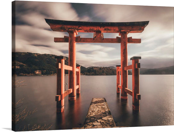 This exquisite print invites you into a serene world where tradition and nature intertwine seamlessly. The vibrant orange Torii gate, a symbol of spirituality and tranquility, stands majestically at the edge of a peaceful lake, creating a harmonious contrast with the muted tones of the surrounding hills and sky. The rugged stone path leading to the gate and the gentle ripples on the water’s surface add depth and emotion to this picturesque view. 