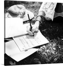  “Woman Writing Down Some Lyrics” invites you into a serene world where creativity blossoms. In this black-and-white masterpiece, a woman sits outdoors, her straw hat resting nearby on the grass. With delicate precision, she writes in an open spiral notebook, pencil poised mid-stroke. 