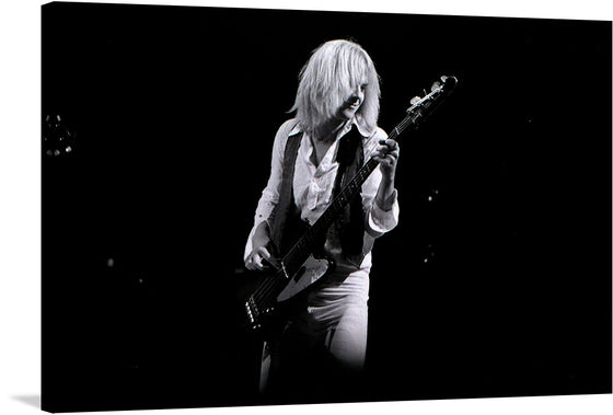 Tom Hamilton of Aerosmith, captured in this iconic black and white photograph at Maple Leaf Gardens in Toronto, 1975, epitomizes the raw energy and soul of rock and roll. His fingers glide across the bass strings, lost in the rhythm, while the stage lights cast dramatic shadows on his face. 