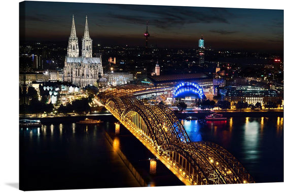 This stunning print of the Cologne Cathedral and Hohenzollern Bridge at night is a must-have for any art lover. The photo-realistic image is taken from a high vantage point, looking down on the city. The cathedral is lit up with white lights, making it stand out against the dark sky.