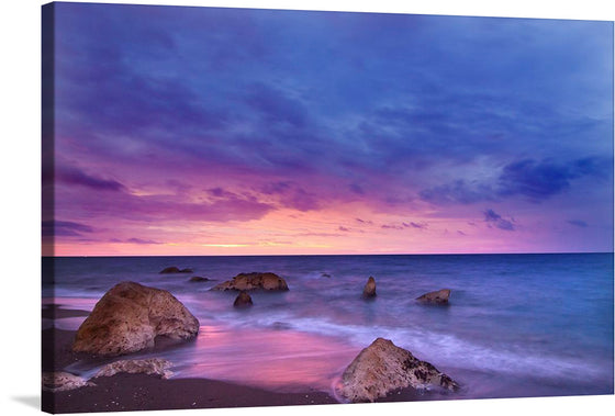 Immerse yourself in the serene beauty of this exquisite print, capturing a tranquil seaside at dusk. The harmonious dance of the vibrant hues of sunset, with purples, pinks, and blues painting the sky, creates a mesmerizing backdrop. The gentle waves kiss the sandy shore where majestic rocks stand as silent witnesses to nature’s awe-inspiring spectacle. 