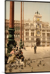 Step into the serene ambiance of a bygone era with this exquisite print. The artwork captures a timeless scene at the iconic St. Mark’s Square in Venice, where elegant architecture, including the renowned Clock Tower, stands as a testament to human ingenuity and artistry. A group of individuals, adorned in period attire, bask in the gentle sunlight, their leisurely poise echoing the tranquil mood.