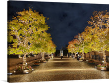  This exquisite print, titled “Illuminations in Ebisu Garden Place,” captures the enchanting atmosphere of a serene evening walkway adorned with trees illuminated by twinkling lights. The golden hues of the leaves, kissed by the gentle embrace of light, contrast beautifully against the tranquil night sky. Every detail, from the cobblestone path to distant figures enjoying the magical setting, invites you into a world where nature and human connection converge in perfect harmony.