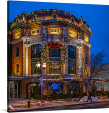   “Place D’Youville, Quebec City, Canada 4.” This artwork captures the enchanting atmosphere of a snowy Canadian evening, where classic elegance meets festive cheer. The ornate building at Place D’Youville is illuminated by soft lighting, highlighting its intricate architectural details. A large Christmas wreath adorned with lights hangs prominently on the front of the building, adding to the festive ambiance. 