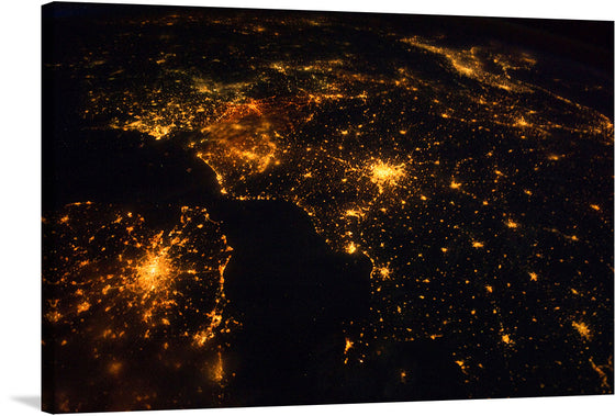 This stunning print titled “Northwestern Europe at Night” is a captivating visual journey that brings the celestial view of our world into your home. The image captures Northwestern Europe as seen from space during nighttime. Bright city lights are prominently visible against a dark backdrop representing landmasses and bodies of water. 