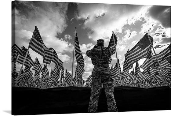 “US Army with American Flags” is a powerful and evocative print that captures a solemn yet inspiring moment. In this black-and-white composition, a soldier stands amidst a sea of stars and stripes, each flag fluttering majestically against an open sky. 
