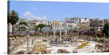  This print features a beautiful panoramic view of the ancient ruins of the Macellum of Pozzuoli in Italy. The ruins are surrounded by modern buildings, creating a unique contrast between the old and the new. The image showcases columns, arches, and walls of the ancient Roman market building, with palm trees and modern buildings in the background.