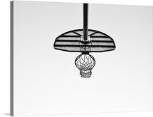  “Below an outdoor basketball net” is a striking black and white photograph of a basketball hoop from below. The image captures the essence of the game, the anticipation of the ball going through the hoop. 
