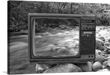  Dive into the serene and surreal world where the past meets the present with our “Old TV” art print. This masterpiece captures a vintage television abandoned, yet beautifully framing a tranquil flowing stream surrounded by nature’s touch. Every detail, from the smooth stones to the gentle flow of water, is encapsulated within the antiquated screen, offering a juxtaposition of technology and nature.