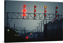  The artwork captures a train station at night, with the red and orange lights of a large metal gantry glowing against the dark sky. The gantry, positioned over a set of train tracks, dominates the scene, while the background reveals a train, power lines, and other buildings. 