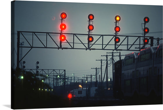 The artwork captures a train station at night, with the red and orange lights of a large metal gantry glowing against the dark sky. The gantry, positioned over a set of train tracks, dominates the scene, while the background reveals a train, power lines, and other buildings. 