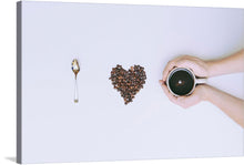  A meticulously arranged heart of rich, brown coffee beans lies between a gleaming spoon and hands tenderly cradling a cup of freshly brewed coffee. Every element is captured with stunning clarity against a pristine white backdrop, evoking a sense of purity and undisturbed tranquility.