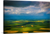 “Landing in France” is a mesmerizing print that offers an aerial perspective of the French countryside. The artwork captures the vast expanse of green fields, divided into geometric shapes, resembling a patchwork quilt of nature. The cultivated lands with varying shades of green and brown create a dynamic palette, enhanced by the dramatic sky overhead. Sunlight pierces through the heavy clouds, casting shadows and illuminating parts of the landscape, adding depth and contrast to the scene.