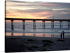 Immerse yourself in the serene beauty of a tranquil sunset by the pier with this exquisite art print. The artwork captures a magical moment where the golden hues of the setting sun paint a masterpiece across the sky, reflecting their warm tones on the gentle waves below. The silhouetted pier stands as a testament to enduring grace amidst nature’s ever-changing canvas. Two figures in the foreground, encapsulated in this moment, add a touch of life’s beautiful impermanence.