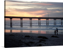  Immerse yourself in the serene beauty of a tranquil sunset by the pier with this exquisite art print. The artwork captures a magical moment where the golden hues of the setting sun paint a masterpiece across the sky, reflecting their warm tones on the gentle waves below. The silhouetted pier stands as a testament to enduring grace amidst nature’s ever-changing canvas. Two figures in the foreground, encapsulated in this moment, add a touch of life’s beautiful impermanence.