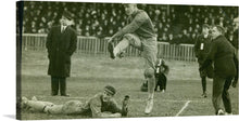  This captivating print captures a riveting moment from an early 20th-century football match. The black and white image is alive with action, featuring players in dynamic movement, their intensity indicative of the high stakes of the game. Spectators, dressed in period attire, add to the historical ambiance, their rapt attention underscoring the excitement of the event.