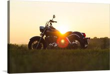  This exquisite print captures a classic motorcycle basking in the golden embrace of the setting sun. The motorcycle, black with chrome details, reflects the warm hues of sunlight, creating an ethereal effect. It’s parked on a grassy field that extends into the distance, meeting a clear sky transitioning from blue to golden hues. 