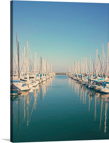  This artwork, titled “Serene Marina,” captures the tranquil beauty of a marina filled with elegant sailboats. The calm waters reflect the masts of the boats, creating a symmetrical visual effect that is both peaceful and captivating. The clear blue sky suggests perfect weather conditions, adding to the overall serenity of the scene. This print is more than just a piece of decor; it’s a window into a world of tranquility and luxury.