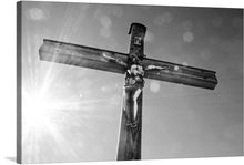  This black and white photo of a Christian cross is a powerful and engaging representation of the essence of Christianity. The cross, made of wood, has a figure of Jesus Christ on it and is in the center of the image with the sun shining behind it.