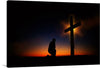 This photo-realistic image of a silhouette of a person kneeling in prayer at the foot of a cross is a peaceful and beautiful representation of the Christian faith. The cross is made of wood and is set against a stunning sunset with a gradient of orange and blue with wispy clouds. 