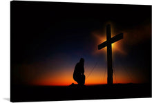  This photo-realistic image of a silhouette of a person kneeling in prayer at the foot of a cross is a peaceful and beautiful representation of the Christian faith. The cross is made of wood and is set against a stunning sunset with a gradient of orange and blue with wispy clouds. 