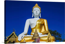  This print features a stunning photograph of a large white and gold Buddha statue in a temple setting. The statue, seated in the lotus position, exudes serenity. Adorned with a gold robe and headpiece, the Buddha is surrounded by smaller gold statues and offerings, creating a scene of reverence and tranquility. 