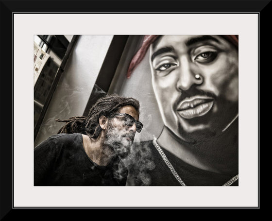 "Man With Dreadlocks and Sunglasses Poses Near Tupac Shakur Portrait"