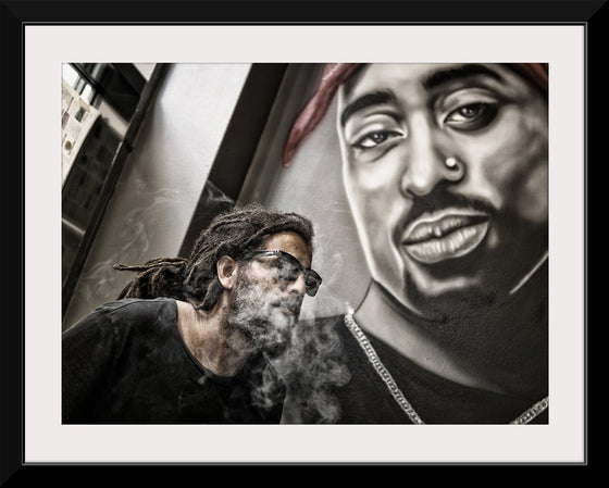 "Man With Dreadlocks and Sunglasses Poses Near Tupac Shakur Portrait"