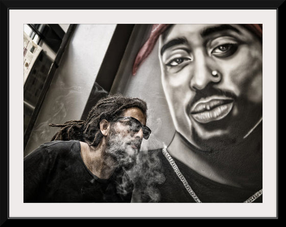 "Man With Dreadlocks and Sunglasses Poses Near Tupac Shakur Portrait"