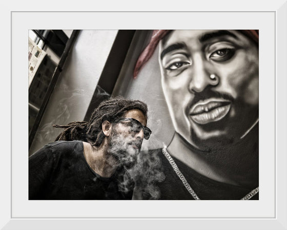 "Man With Dreadlocks and Sunglasses Poses Near Tupac Shakur Portrait"