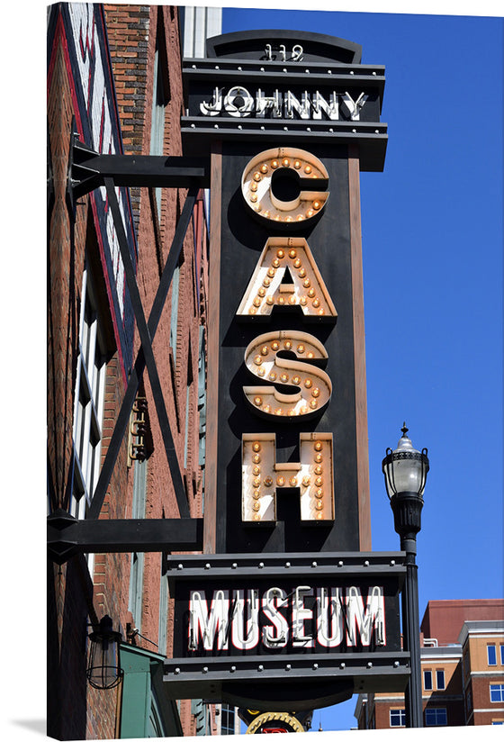 This artwork is a stunning print of the Johnny Cash Museum sign. The sign features a tall vertical design with “119 JOHNNY” in white letters against a black background at the top. Below that, “CASH” is spelled out in large capital letters adorned with illuminated marquee bulbs. At the bottom, “MUSEUM” is written in white capital letters on another black rectangular background. 