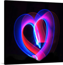  This print is a captivating piece of art that brings a touch of modern aesthetics to any space. It features a heart shape, crafted from vibrant blue and pink light trails against a stark black background. The heart, slightly off-center, adds a dynamic element to the composition.
