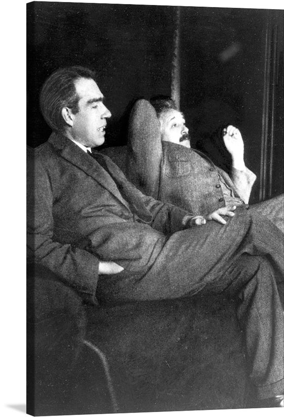This is black and white photograph of Albert Einstein and Niels Bohr sitting on a couch. The men are both wearing suits and ties, and they appear to be in deep conversation. Albert Einstein is on the left smoking a cigarette, and Niels Bohr is on the right looking at him intently.