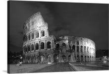  “Outside of Colosseum in Rome, Italy” is a stunning black and white photograph that captures the grandeur of ancient Rome. The Colosseum’s intricate architecture, with its arches and partial ruins, is highlighted under artificial lighting. Dark clouds are visible in the sky above, adding a dramatic effect to the scene. 