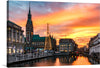 This print brings to life the majestic architecture, with the iconic clock tower standing tall amidst beautifully constructed buildings, each telling tales of a rich historical tapestry. A Christmas tree, adorned with twinkling lights, adds to the festive spirit and contrasts harmoniously with the warm hues of the sunset painting the skies. The calm waters reflect this magical scene, offering a tranquil escape within an urban setting.