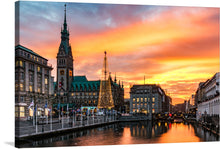  This print brings to life the majestic architecture, with the iconic clock tower standing tall amidst beautifully constructed buildings, each telling tales of a rich historical tapestry. A Christmas tree, adorned with twinkling lights, adds to the festive spirit and contrasts harmoniously with the warm hues of the sunset painting the skies. The calm waters reflect this magical scene, offering a tranquil escape within an urban setting.