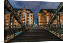  Immerse yourself in the enchanting allure of this exquisite print capturing a serene night at the iconic warehouse district, Speicherstadt in Hamburg. This artwork encapsulates the harmonious blend of historic architecture and modern illumination, offering a visual journey through the wooden bridge that leads to majestic brick buildings adorned with elegant windows.