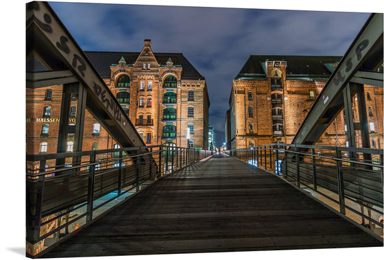 Immerse yourself in the enchanting allure of this exquisite print capturing a serene night at the iconic warehouse district, Speicherstadt in Hamburg. This artwork encapsulates the harmonious blend of historic architecture and modern illumination, offering a visual journey through the wooden bridge that leads to majestic brick buildings adorned with elegant windows.