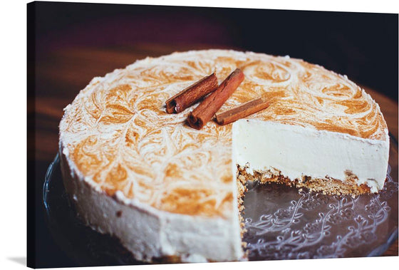 he image is a photo-realistic representation of a cinnamon cheesecake with a slice cut out. The cheesecake is on a glass plate with an intricate design. The top of the cheesecake has a beautiful swirl pattern, and two cinnamon sticks are placed on top of it. 