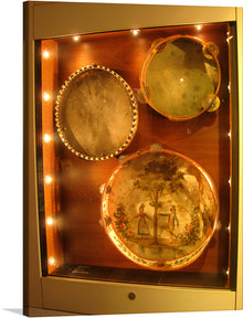  This exquisite print is a meticulous recreation of vintage percussion instruments showcased in a well-lit display. The centerpiece is an ornate percussion instrument depicting two figures amidst lush greenery under an overcast sky, evoking a sense of timeless beauty and grace. The surrounding border of this percussion instruments is detailed with intricate designs enhancing its antique aesthetic. 