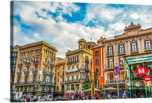  This colorful and captivating print captures the vibrant essence of a bustling Barcelona street. The ornate, colorful buildings stand tall against a clear blue sky, their intricate details inviting you to explore every nook and cranny. As sunlight filters through the leaves, people and cars move with purpose, creating a lively rhythm.